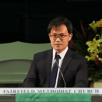 Formal man in suit and glasses speaking at Fairfield Methodist Church event.