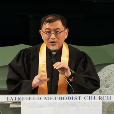 Elderly pastor speaking at Fairfield Methodist Church worship service; religious leader delivering sermon.