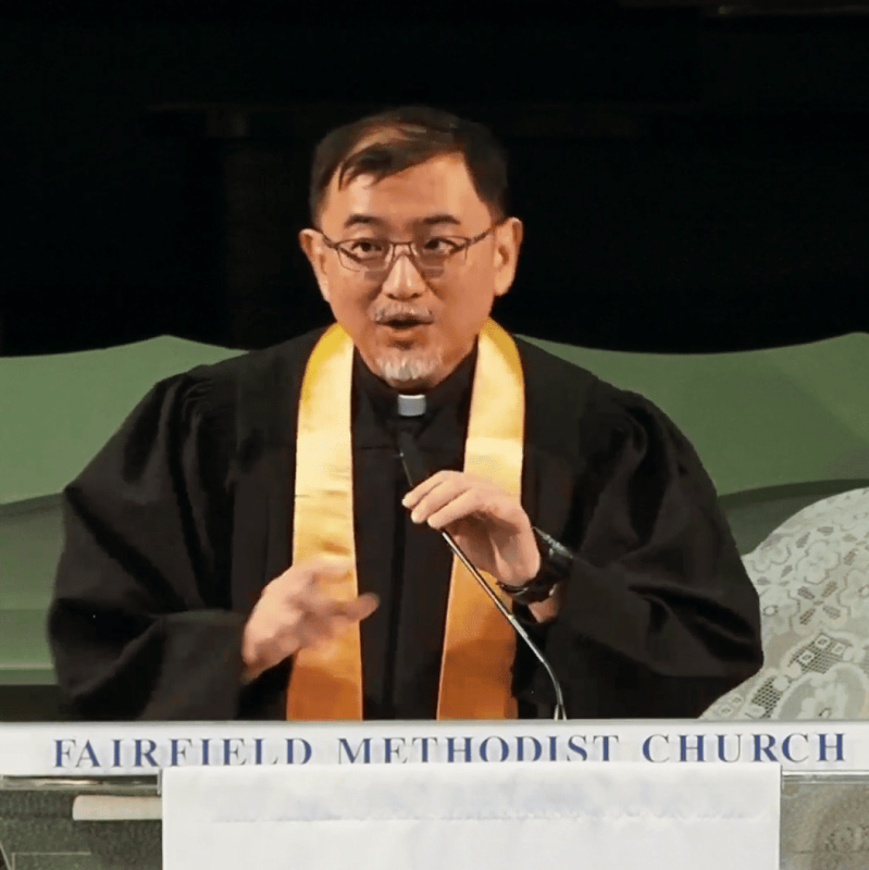 Elderly pastor speaking at Fairfield Methodist Church worship service; religious leader delivering sermon.