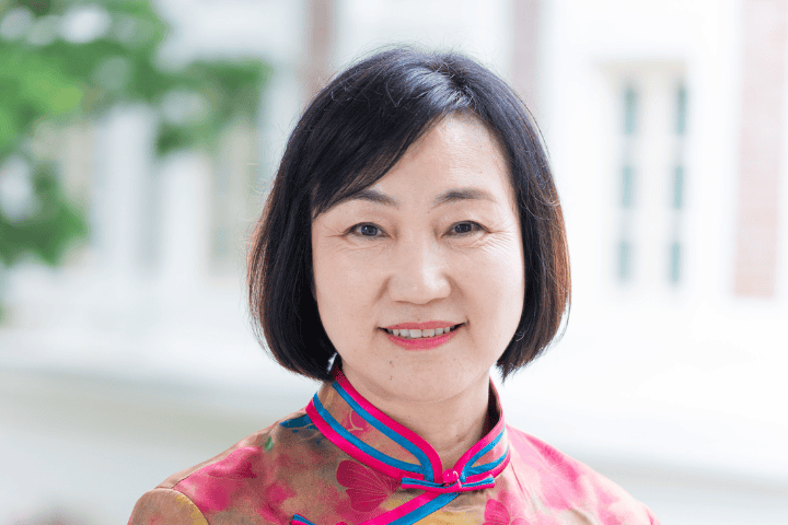Senior Asian woman smiling in traditional Chinese dress, outdoor background.